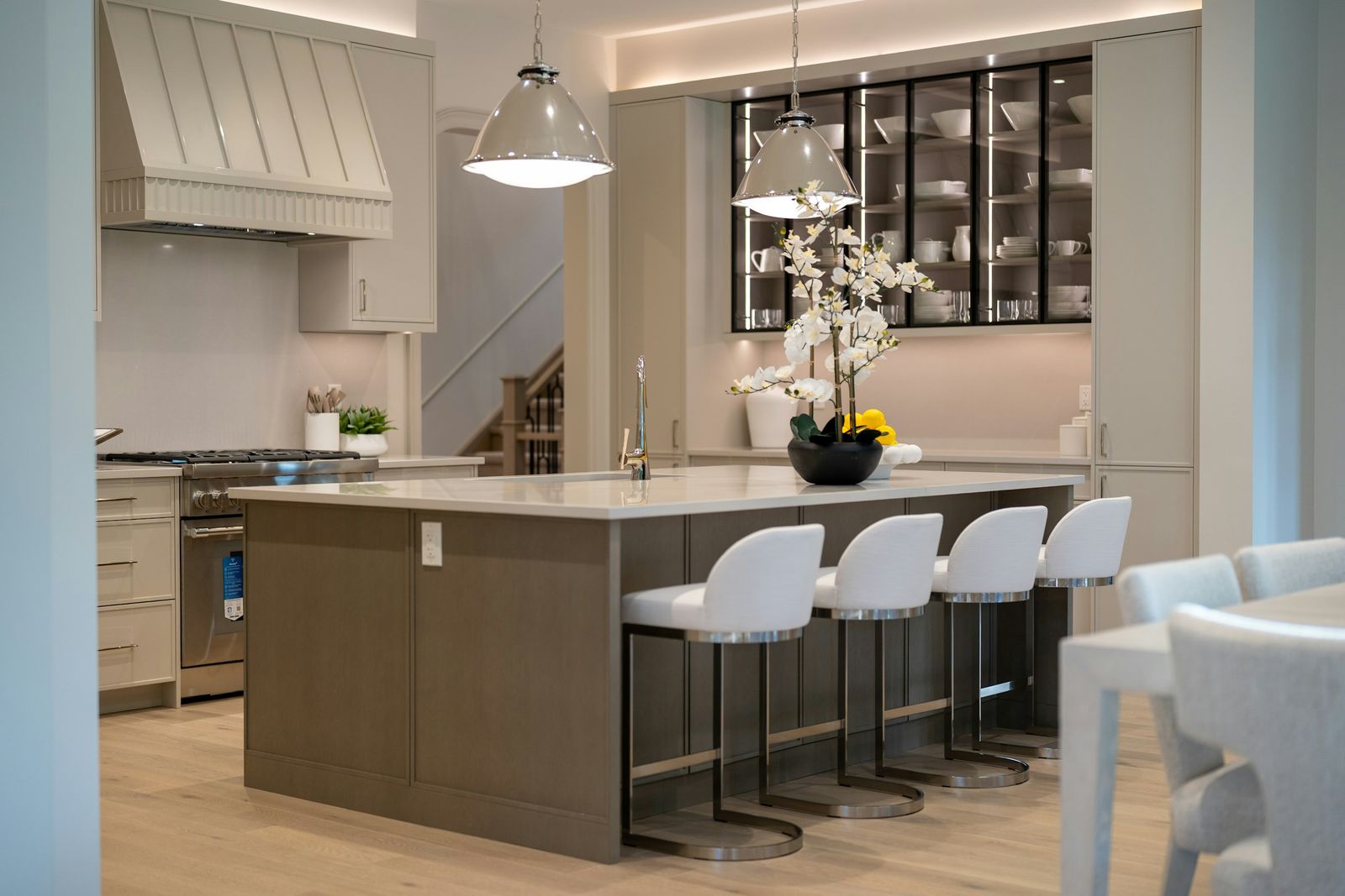 Modern kitchen with cove lighting above the cabinets, LED-lit glass-front cabinets, under-cabinet lighting and two polished nickel dome pendants over a taupe island