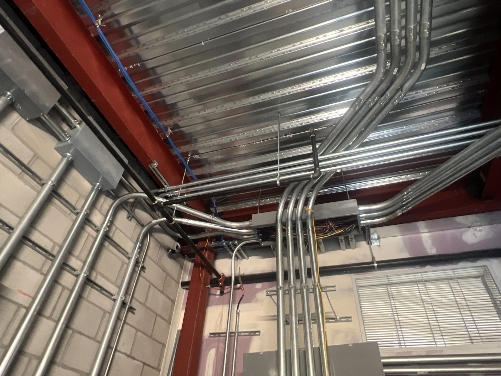 Parallel runs of EMT conduit with matched bends crossing a steel roof deck and dropping down a block wall into junction boxes